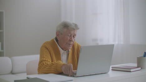 Senior-woman-with-laptop-computer-calling-on-smartphone-at-home.-Old-woman-having-a-video-call-on-the-laptop-smiling-and-talking-happily-indoors-in-a-cozy-apartment.-doctor-video-calling-older-patient